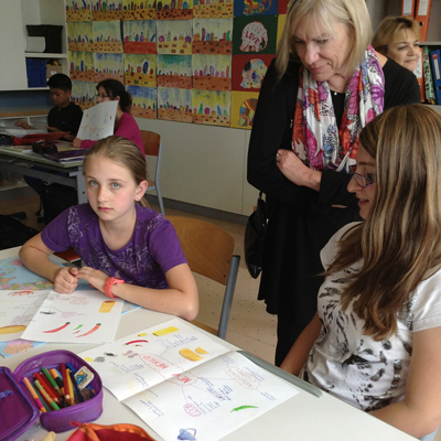 Deborah Rifenbary, UNM College of Education associate dean and coordinator of the STARS program, looks over the shoulder of Austrian schoolchildren as they create posters depicting New Mexico.